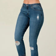 Blue jeans with distressed details worn by a person on a plain background