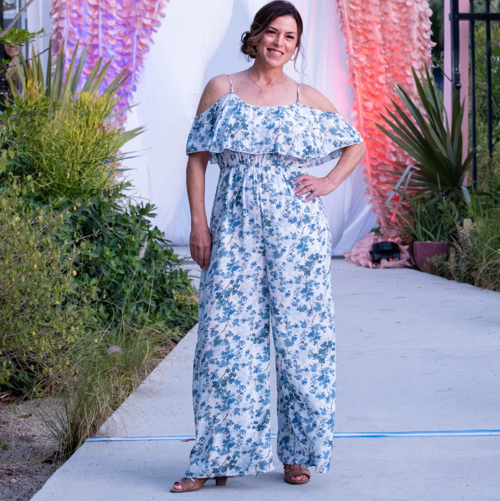 Woman in a floral off-shoulder jumpsuit standing in front of a 'Village Square Islamorada' backdrop.