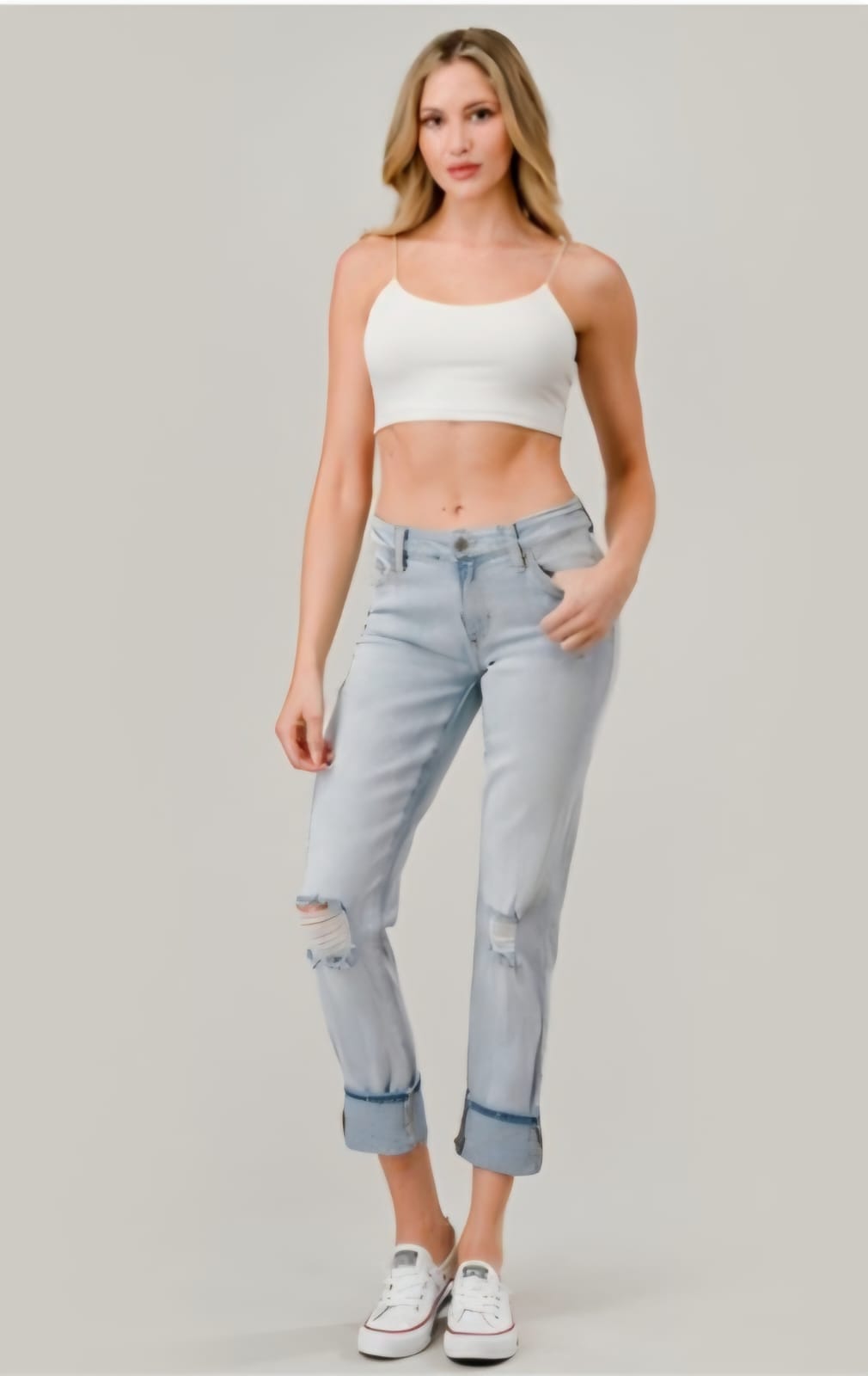 Woman wearing a white crop top and light blue jeans on a plain background