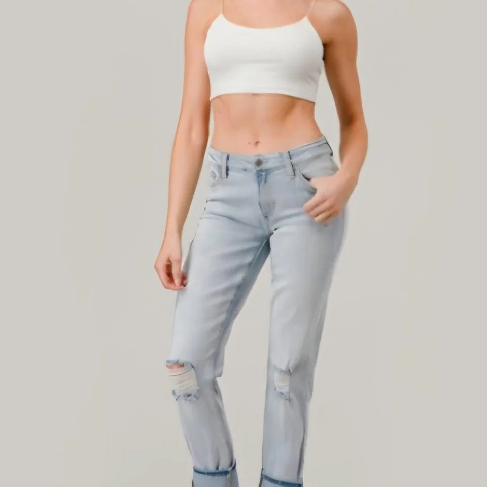 Woman wearing a white crop top and light blue jeans on a plain background